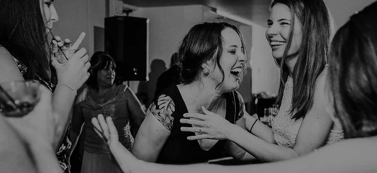 black and white faded picture of girls laughing and drinking at a wedding reception