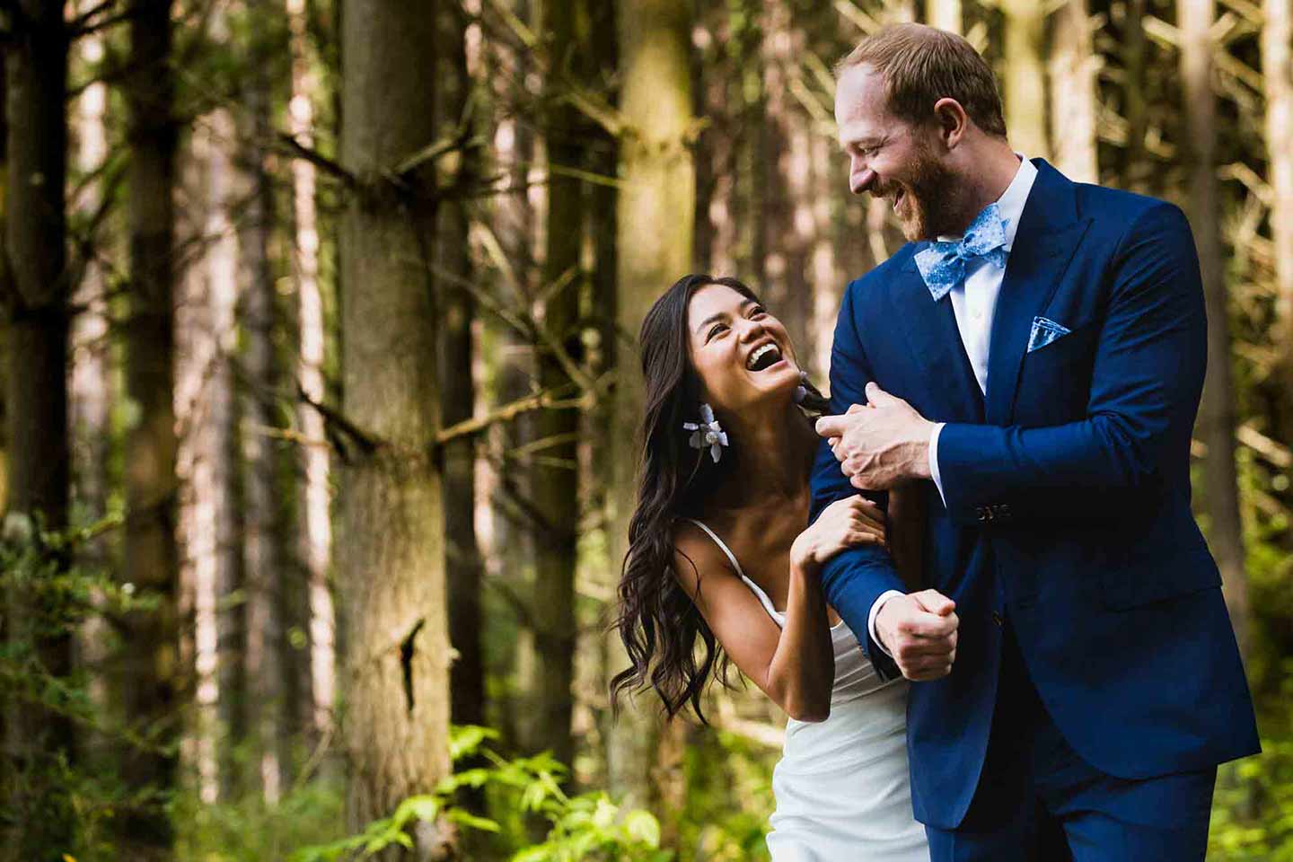 bride and groom laughing together and walking in the woods
