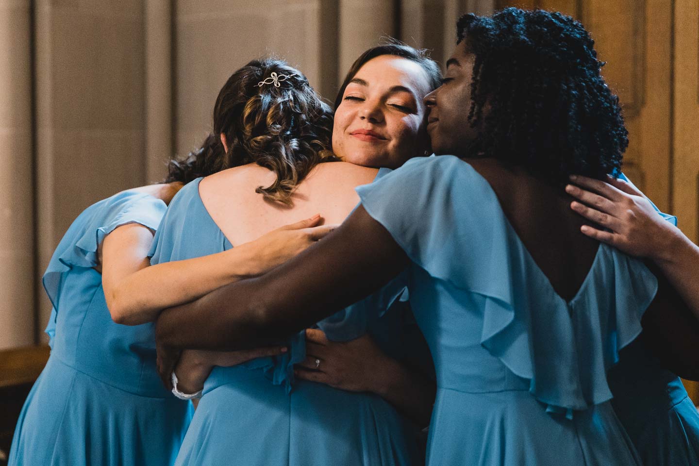 bride hugs her girls in blue bridesmaid dresses, all together while smiling with her eyes closed
