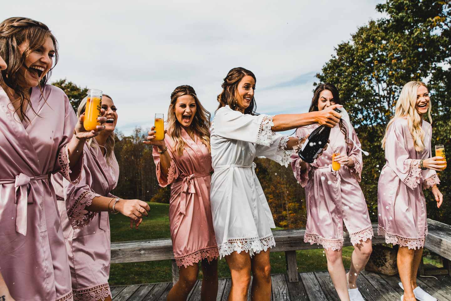 bride pops a cork on the champagne, making a mess surrounded by her laughing bridesmaids